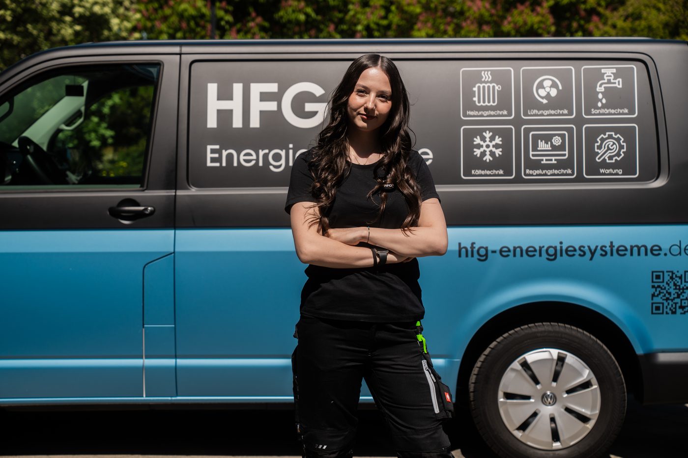 Mitarbeiterin von HFG+ mit verschränkten Armen vor einem blauen Firmenbus