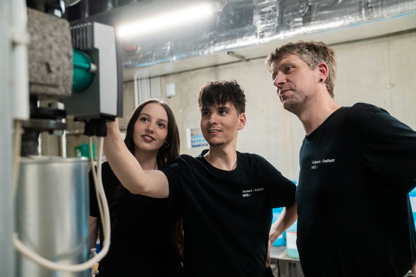 Drei Mitarbeiter von HFG+ besprechen sich an einem Gerät im Technikraum